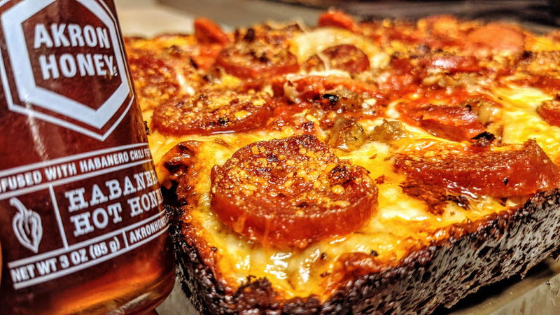 Habanero hot sauce bottle next to a pizza with pepperoni slices