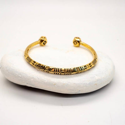 An etched and decorated brass bangle with intricate patterns, displayed on a rock-like surface.